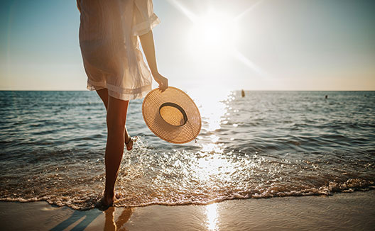 Woman walking on beach with sun hat